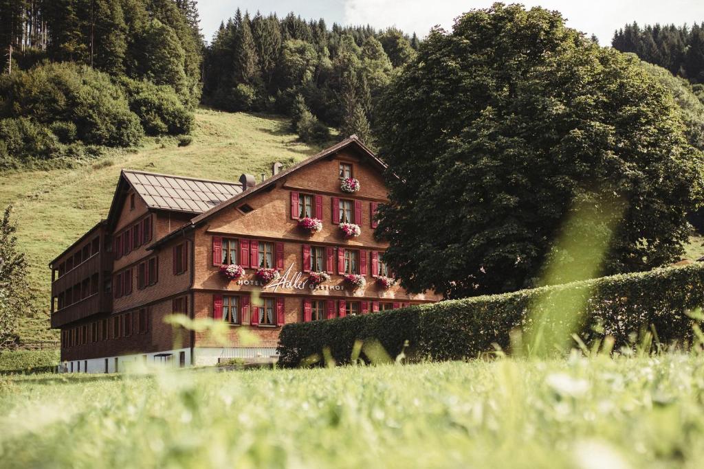 a building on a hill in a field with trees at Hotel Gasthof Adler in Schoppernau