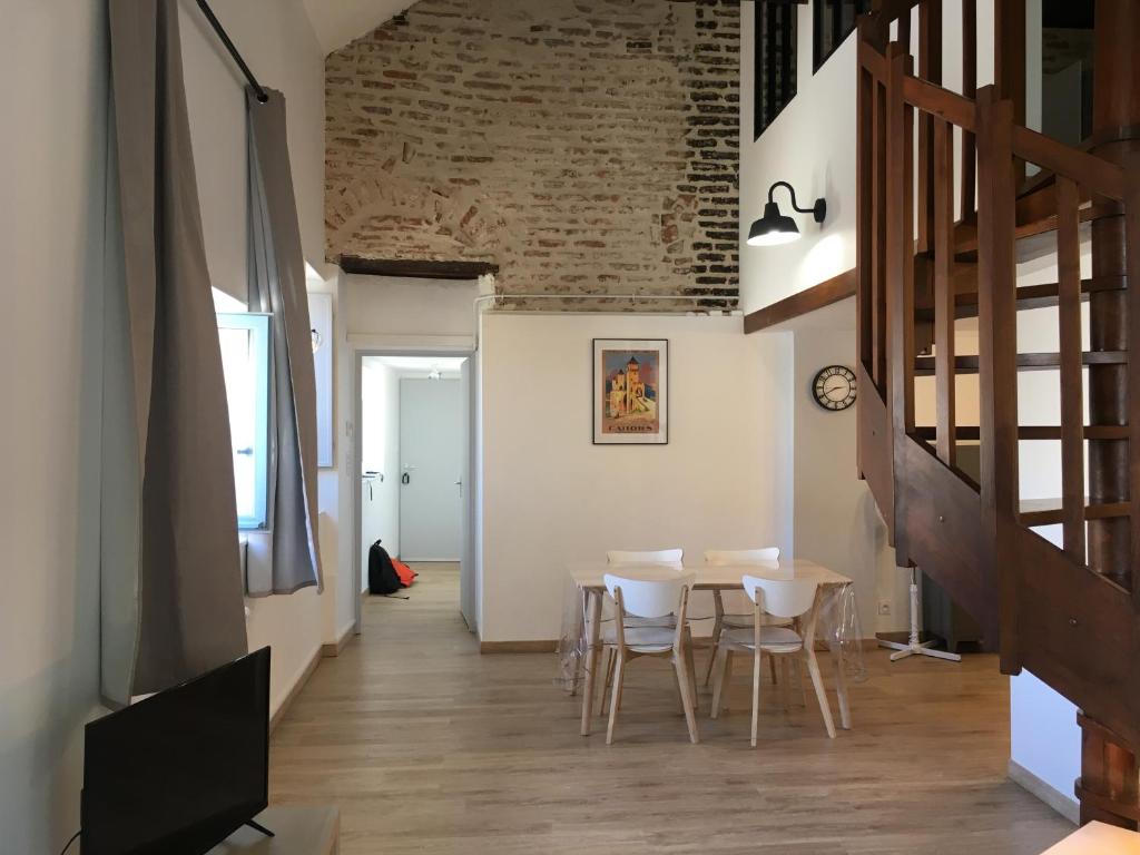 Le Loft Du Chateau Du Roi في كاهور: غرفة طعام مع طاولة وكراسي وجدار من الطوب