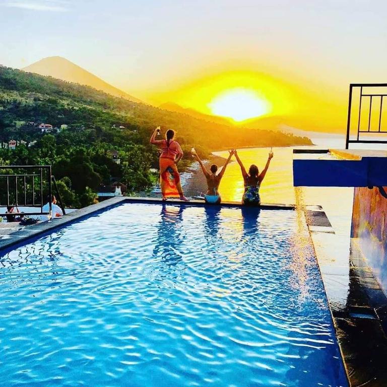 a group of people jumping into a swimming pool with the sunset at Waenis Sunset View Hotel and Restaurant, Amed, Bali in Amed