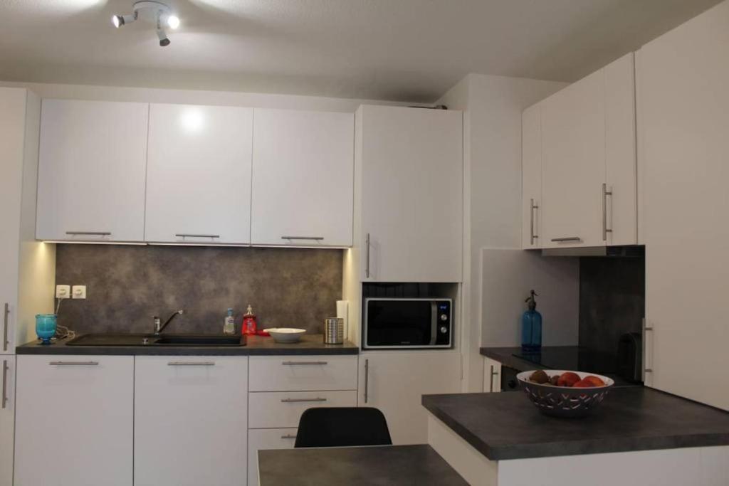 a kitchen with white cabinets and a bowl of fruit on a counter at ZIBURU TERRASSE PARKING TOUT A PIED SAINT JEAN DE LUz in Ciboure