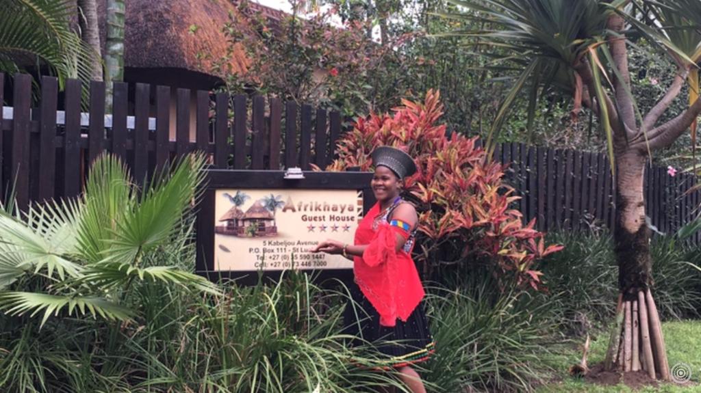 una mujer con un vestido rojo de pie junto a una señal en Afrikhaya Guest House, en St Lucia