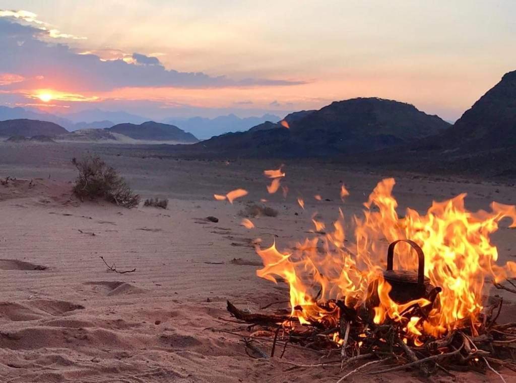 a bonfire in the desert with mountains in the background at WADI RUM-Bedouin Tents and Jeep Tours in Wadi Rum