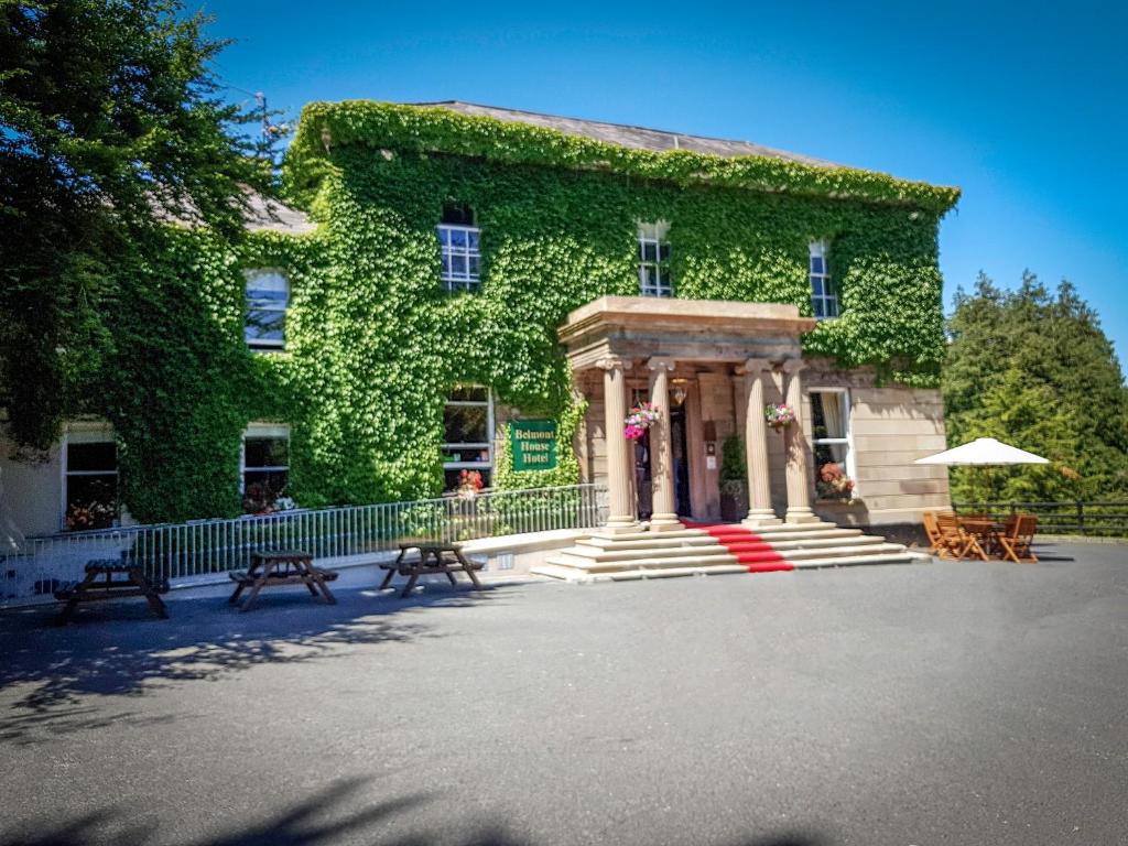 a building covered in ivy with benches in front of it at Belmont House Hotel in Banbridge