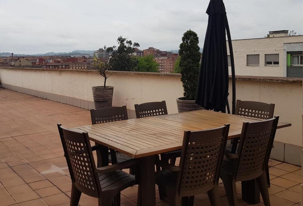 a wooden table with chairs and an umbrella on a roof at Lauredal - Ático con amplia terraza, 2 hab, 2 baños, pádel, parque infantil in Gijón
