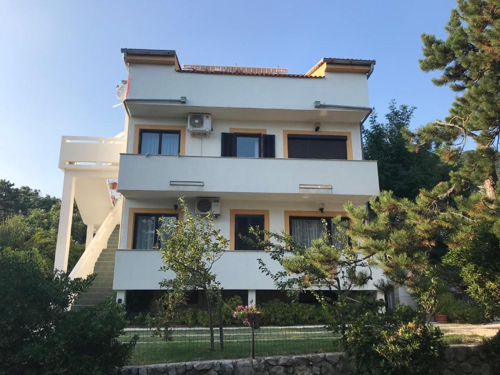 une maison blanche avec des arbres devant elle dans l'établissement Apartments Lena, à Baška