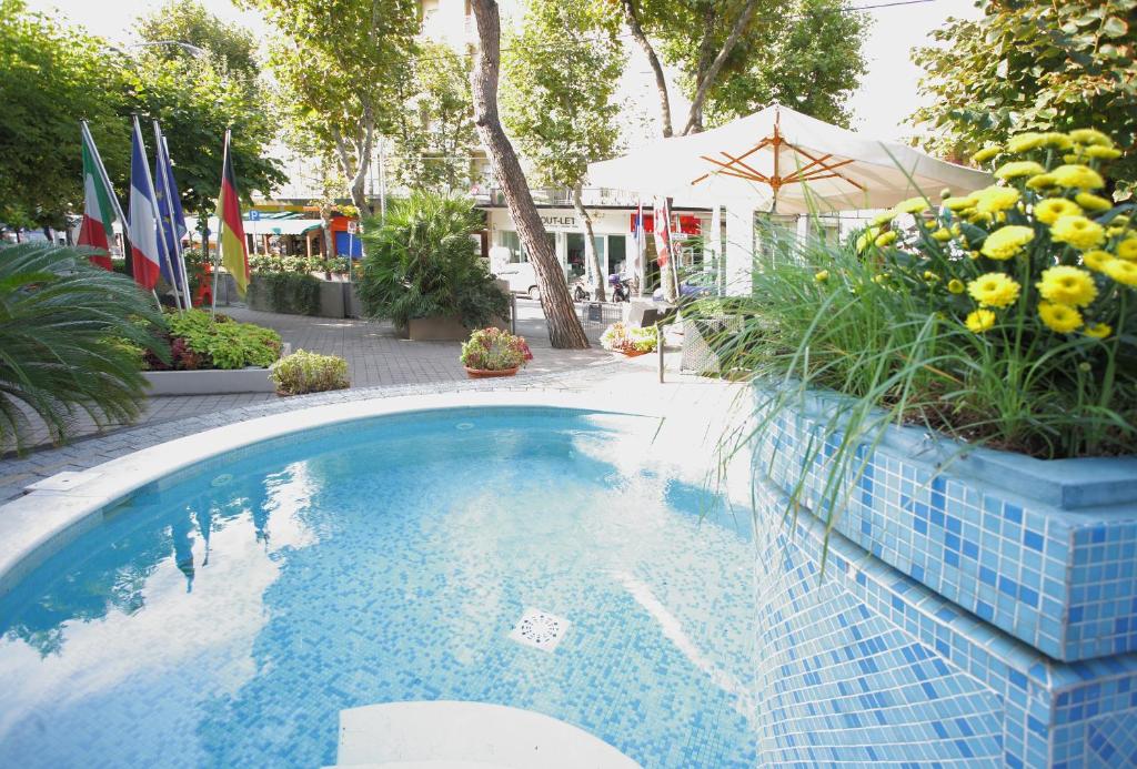 - une piscine dans un complexe avec drapeaux et plantes dans l'établissement Hotel Derby, à Rimini