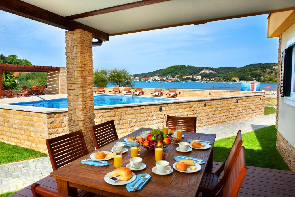 een houten tafel met eten op een patio met een zwembad bij Lando Resort in Rab