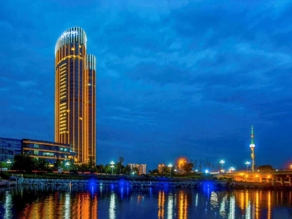 a tall building next to a river at night at Pullman Linyi Lushang in Linyi