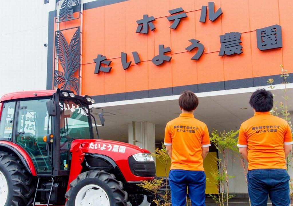 dos hombres parados frente a un edificio con un tractor en Hotel Taiyo Nouen Furumitsu en Matsuyama