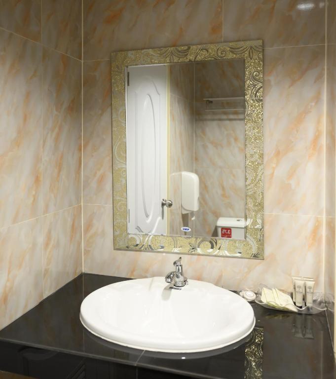 A compact vanity with a white basin, black countertop, and ornate framed mirror.