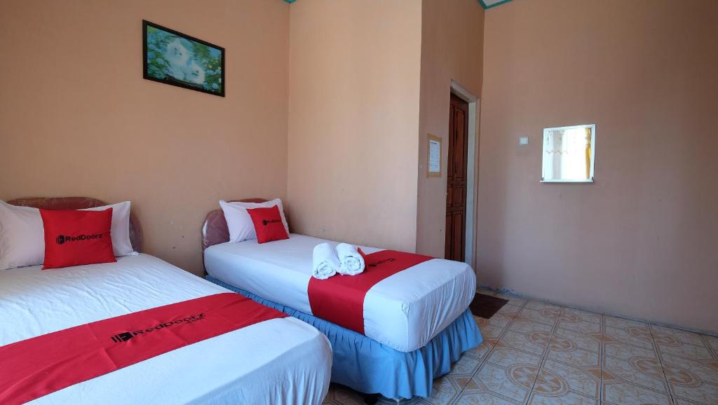 Habitación con 2 camas y sábanas rojas y blancas. en RedDoorz near Mangrove Forest Kupang, en Kupang