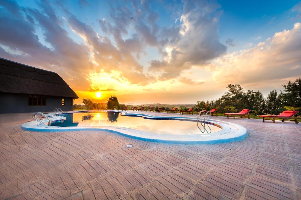 a swimming pool with a sunset in the background at Emburara Farm Lodge in Mbarara