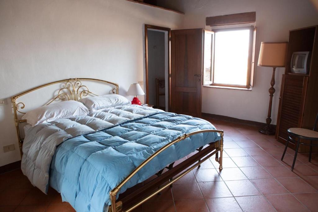 a bedroom with a bed with a blue comforter and a window at La Fattoria Montalcinello in Chiusdino
