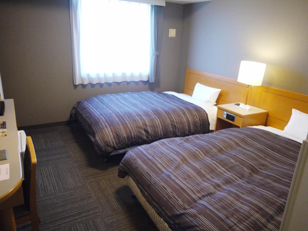 a hotel room with two beds and a window at Hotel Route-Inn Niigata Kencho-minami in Niigata