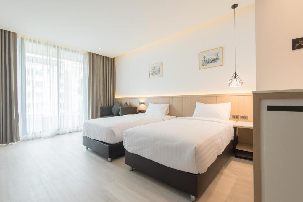 A bright twin room with two beds, a small desk and a full-height curtained window.