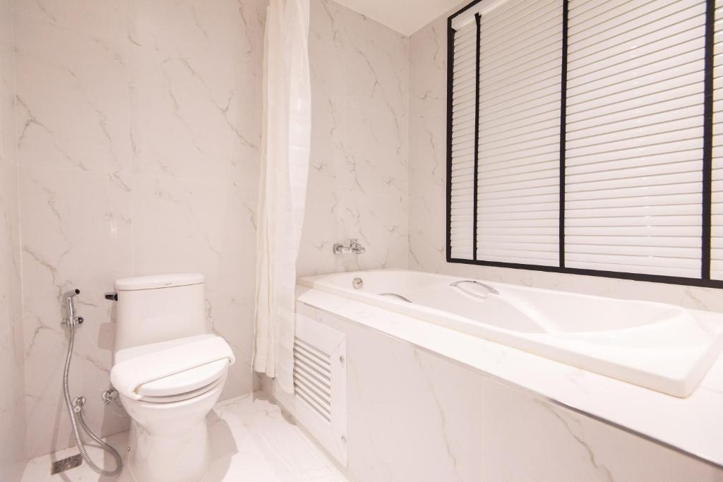 A white marble-look bathroom with a toilet, handheld bidet spray and built-in bathtub.