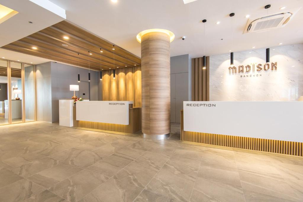 A bright hotel reception lobby with two front desks and the Madison Bangkok sign.