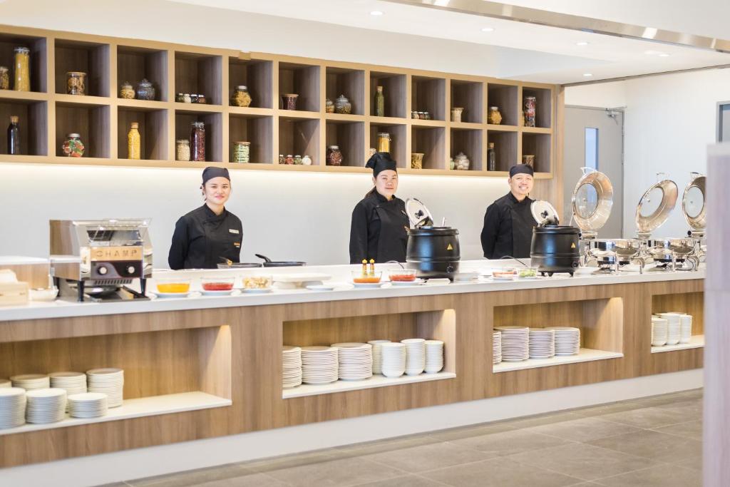 A staffed buffet counter with three chefs, hot pots, plates and display shelving.