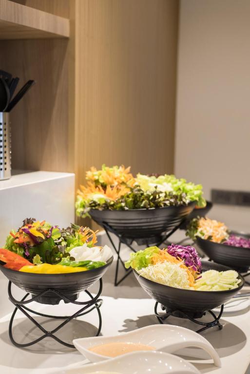 A salad and vegetable station with dressed greens, shredded vegetables, and sauces.