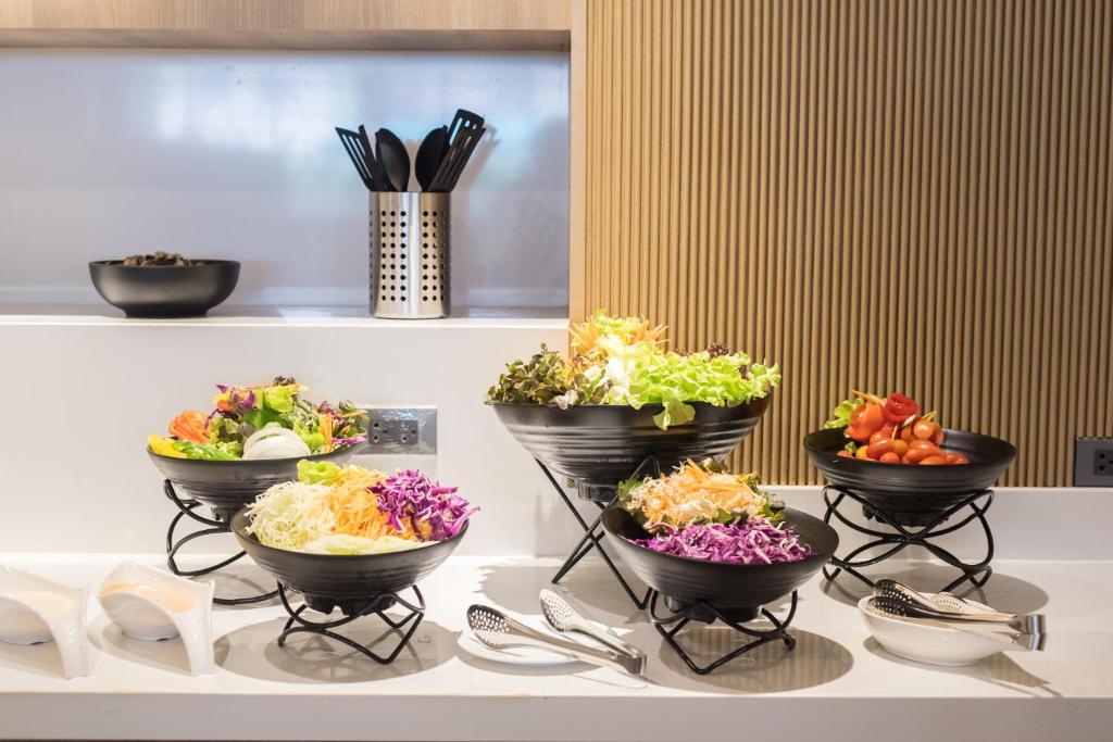 A broad salad buffet with leafy greens, cabbage, tomatoes, and serving utensils.