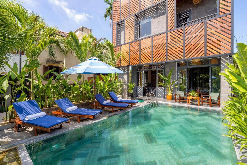 ホイアンにあるTropical Home Villaの建物の隣に椅子とパラソルのあるプール