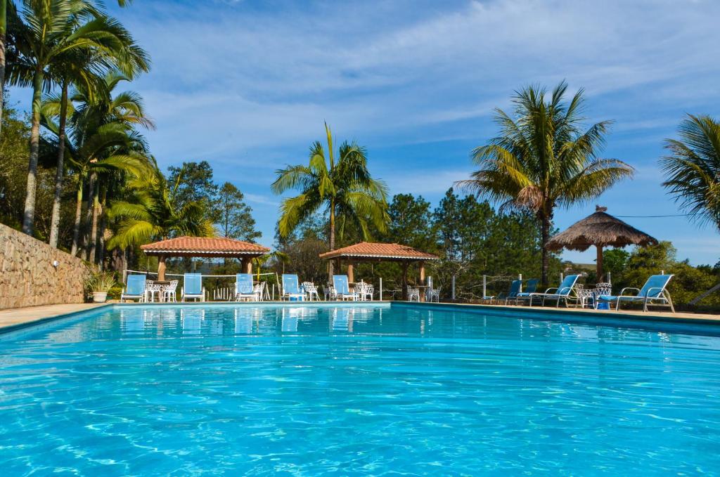 a swimming pool with chairs and palm trees at Hotel Fazenda Villa Galicia in Nazaré Paulista