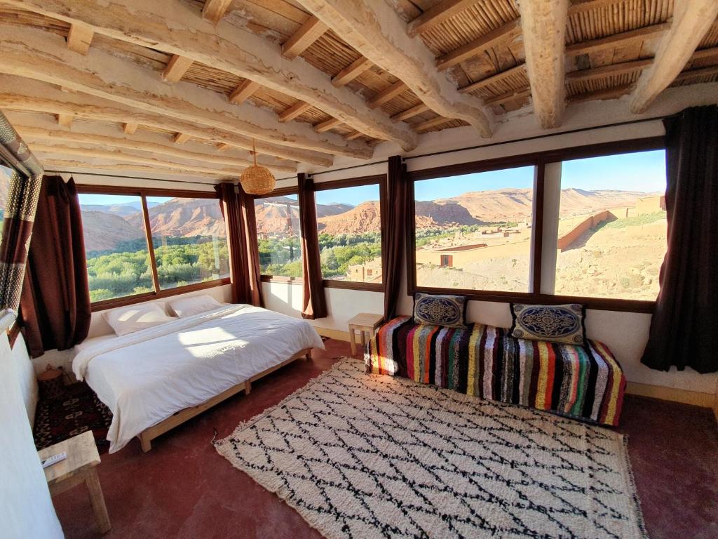 a bedroom with a bed and a couch and windows at Kasbah Chems in El Kelaa des Mgouna