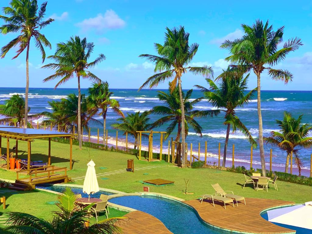 a resort with a pool and palm trees and the ocean at Apartamento beira-mar no Bali Bahia in Itacimirim