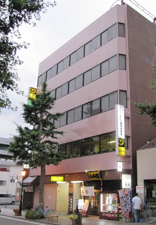 un edificio rosa con un árbol delante de él en Ito Station Hotel, en Ito