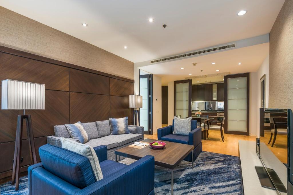 A spacious suite living room with blue seating, television and an open kitchen-dining area.