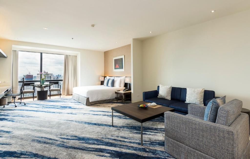 A bright open-plan suite with a bed, sofa, and city-facing window.