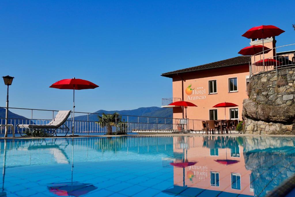 una piscina con sombrillas rojas y un edificio en Hotel Arancio, en Ascona