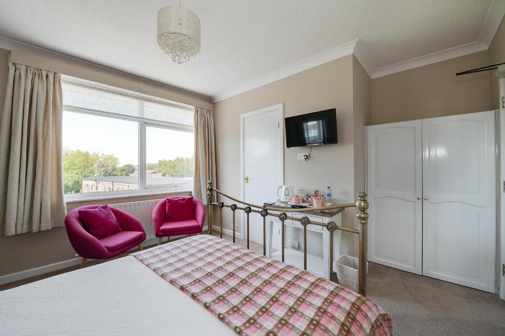 a bedroom with a bed and two pink chairs at The Coast Yard B & B and Garden Chalets in Selsey