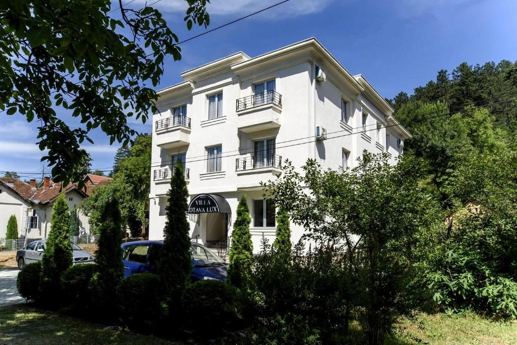 un edificio blanco con un coche aparcado delante de él en Villa Otava Lux SPA, en Vrnjačka Banja