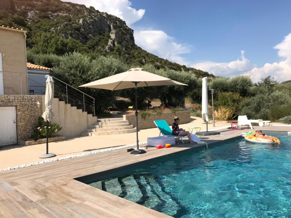 una persona sentada en una silla junto a una piscina con sombrilla en Luxury air-con Villa, heated pool, stunning views, nearby a lively village, en Volx