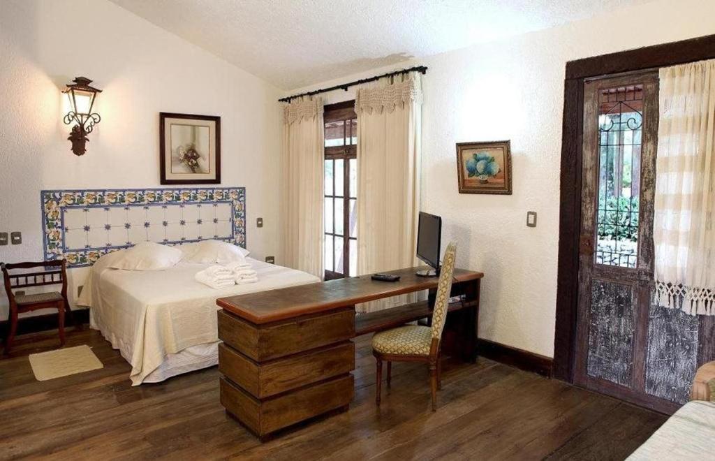 a bedroom with a bed, chair, table and window at Pousada Solar dos Vieiras in Juiz de Fora