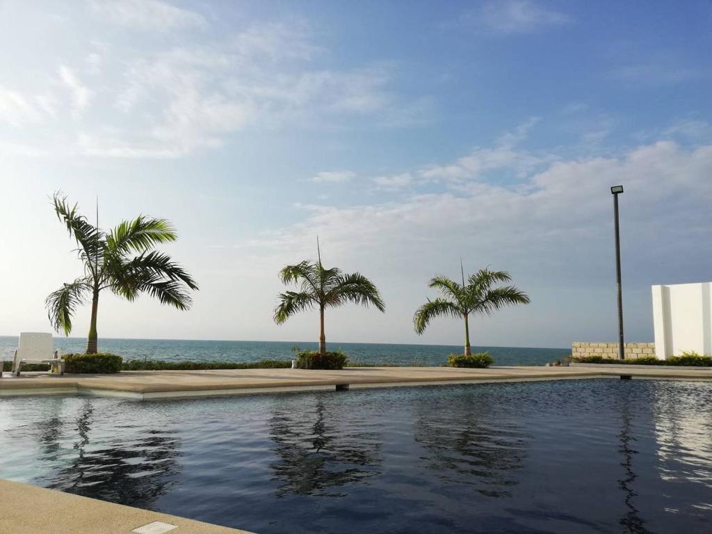 a swimming pool with palm trees and the ocean at Dpto Moderno Frente al Mar. Edf: Deymar 7mo Piso in Tonsupa