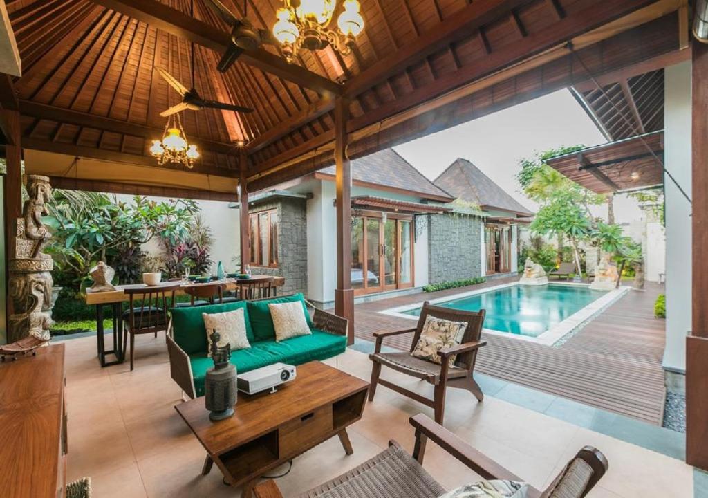 an outdoor living room with a green couch and a pool at Villa Niketan Sanur - Three bedroom in Sanur