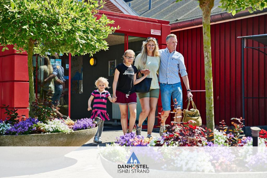 une famille debout en face d'un bâtiment rouge avec des fleurs dans l'établissement Danhostel Ishøj Strand, à Ishøj