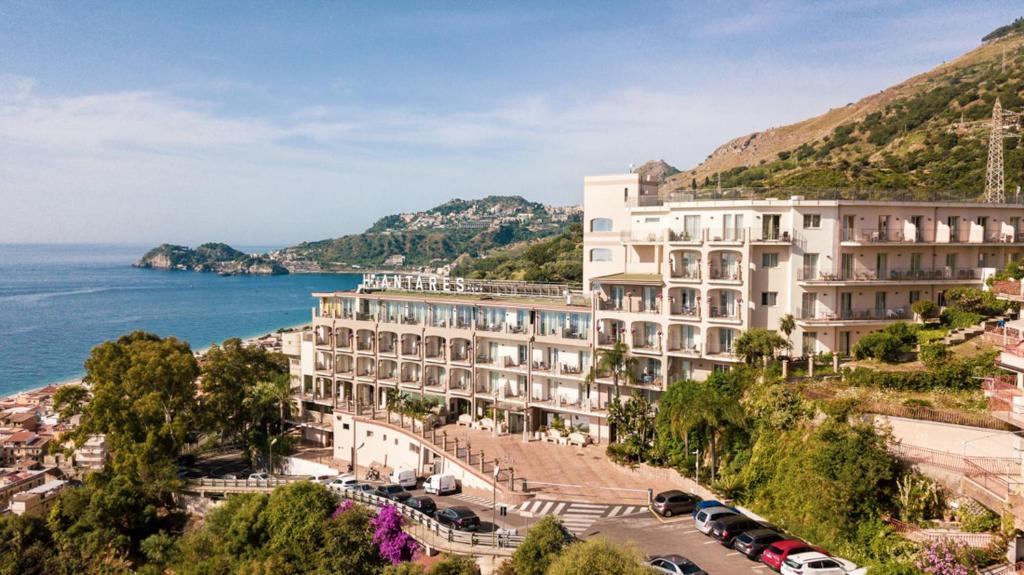 a large white building on a hill next to the ocean at Hotel Antares in Letojanni