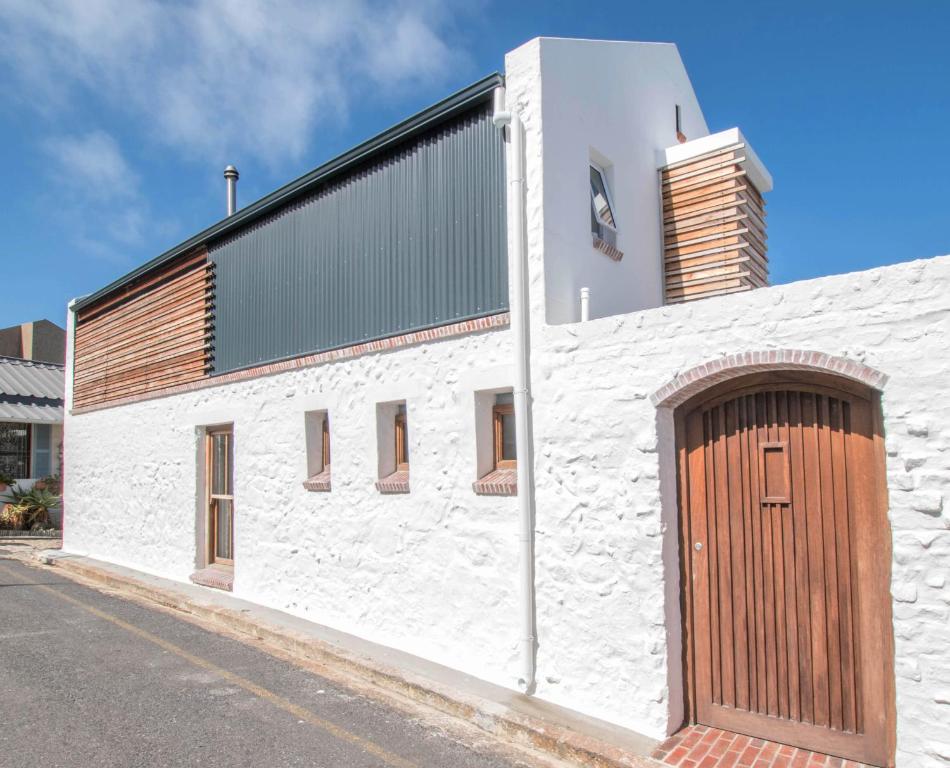a white building with a wooden door on the side of it at Rosmead Apartment in Kalk Bay