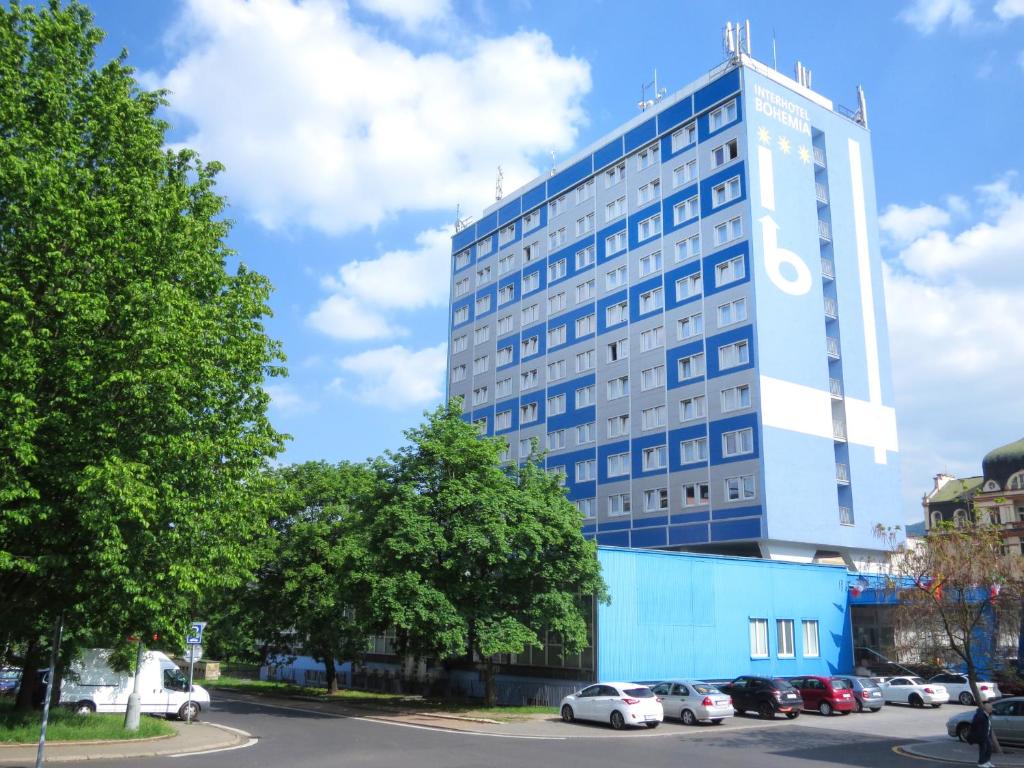 拉贝河畔乌斯季波西米亚泰尔酒店的一座高大的蓝色建筑,前面有汽车停放