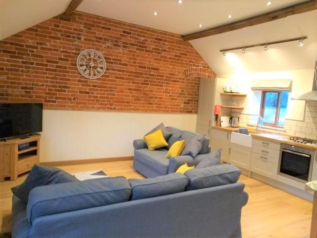 ein Wohnzimmer mit einem blauen Sofa und einer Ziegelwand in der Unterkunft Blashford Manor Holiday Cottage - The Dartmoor Cottage in Ellingham