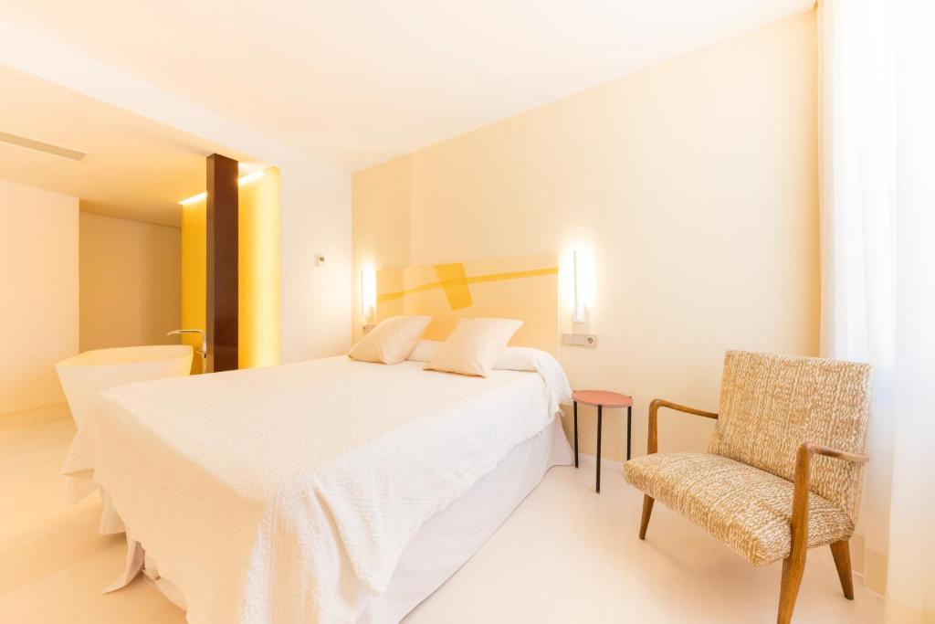 a white bedroom with a bed and a chair at Fonda Llabres Boutique in Alcudia