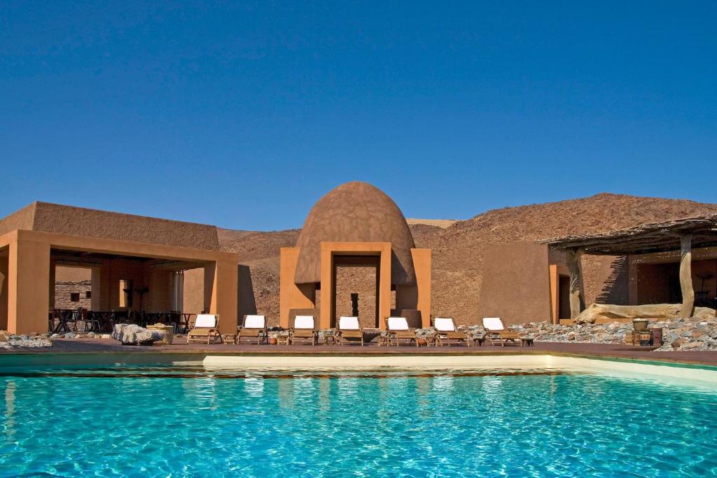 a resort with a pool with chairs and a building at Okahirongo Elephant Lodge in Purros