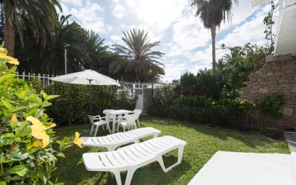 un patio con 2 panche bianche e un ombrellone di Bonito Bungalow a pocos metros de la playa a Puerto Rico de Gran Canaria
