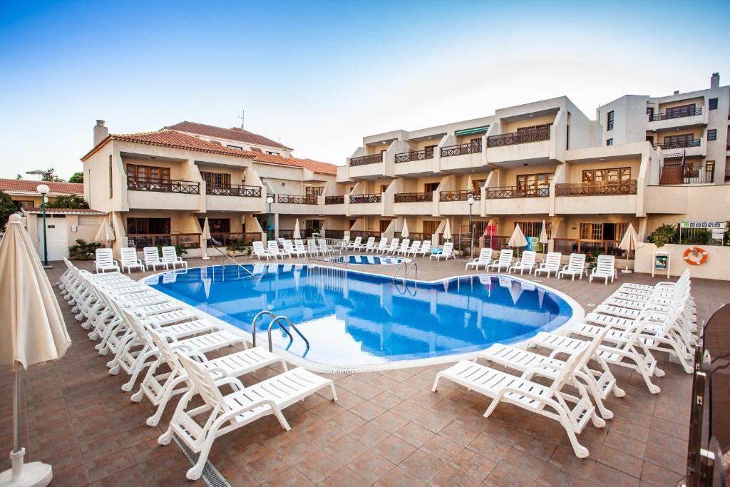 uma piscina com espreguiçadeiras brancas em frente a um hotel em Spectacular Ocean Apartment with AirCon in Golden Mile of Las Americas em Arona