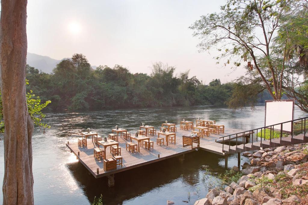 un grupo de mesas y sillas en un muelle sobre un río en Mida Resort Kanchanaburi - SHA PLUS, en Sai Yok