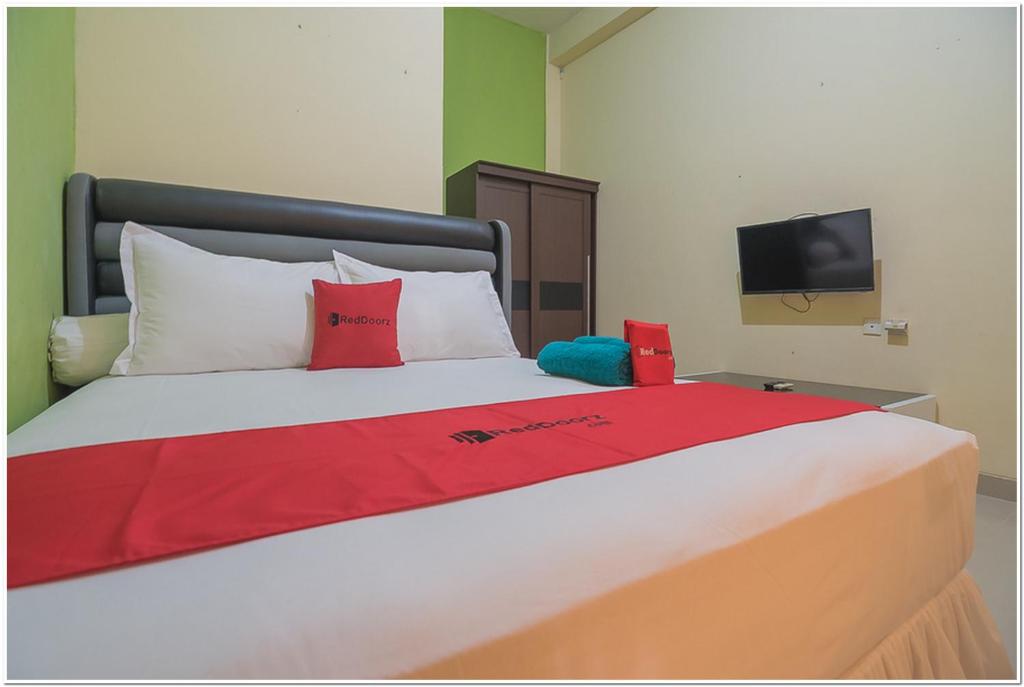 a bed with red and white pillows and a tv at RedDoorz near Lapangan Tenis Balikpapan in Balikpapan