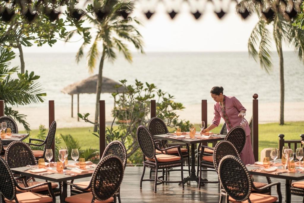 a woman standing at a table in front of the ocean at Four Seasons Resort Langkawi in Tanjung Rhu